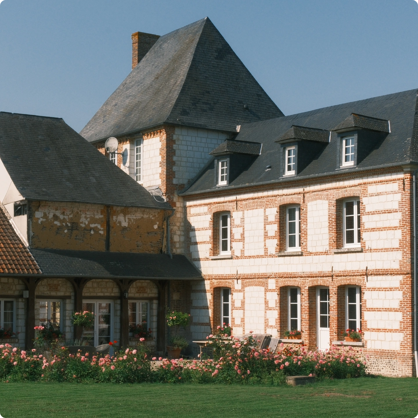 Manoir en brique et pierre au toit d'ardoise pentu et jardin de roses