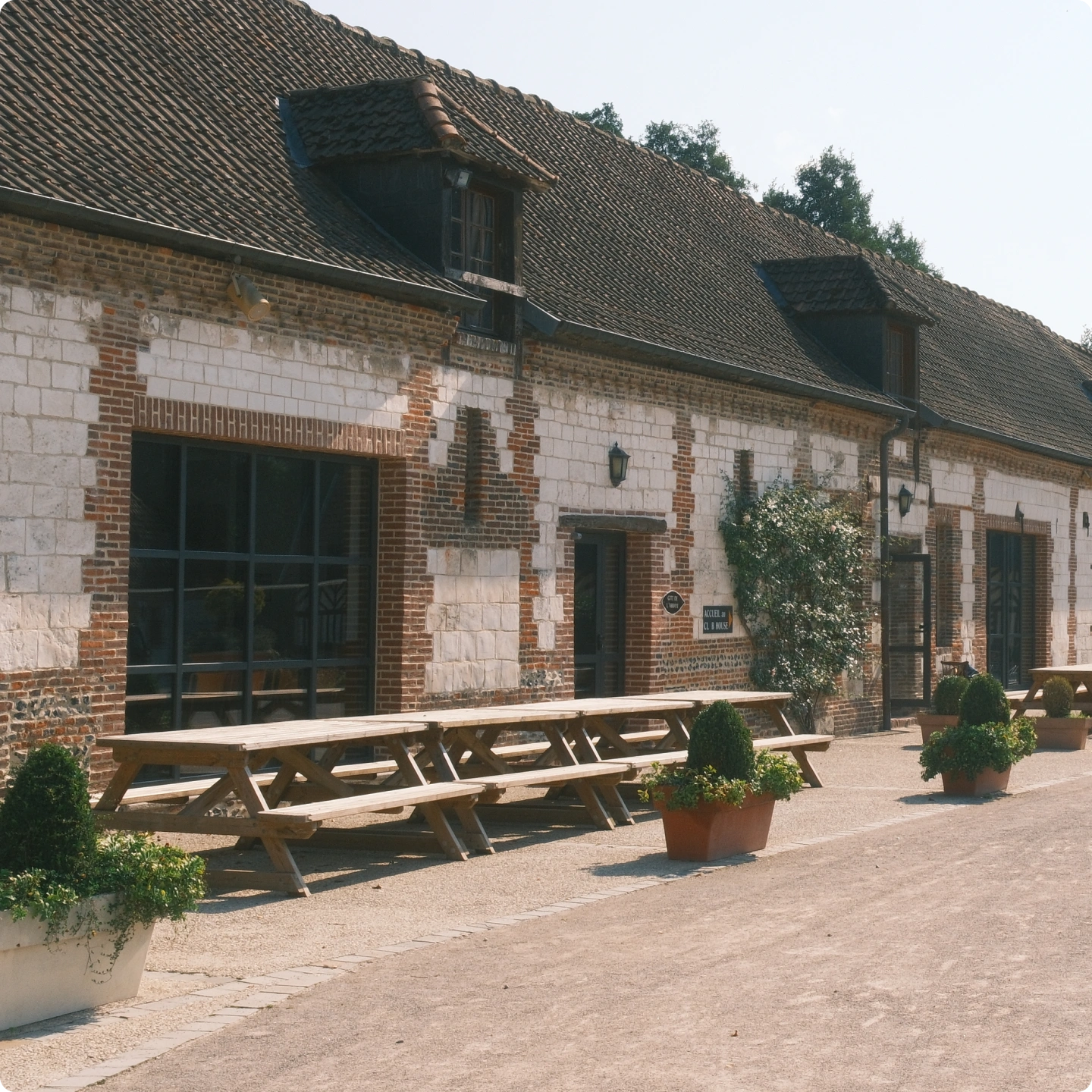 Bâtiments de ferme en pierre et brique aux toits de tuiles, tables de pique-nique