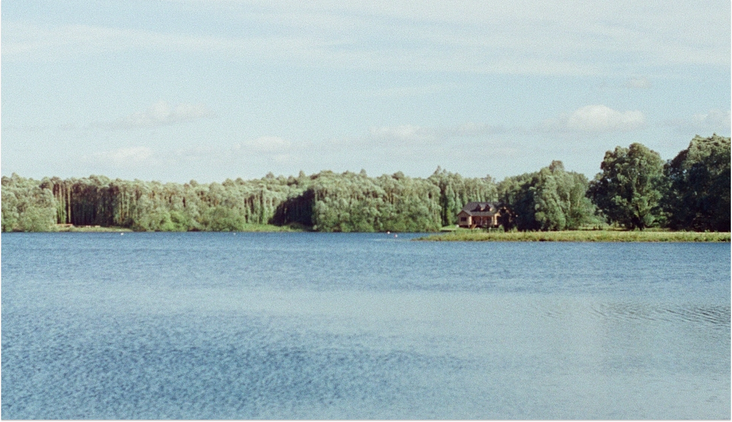 Étang bordé de forêt avec une maison sur la rive