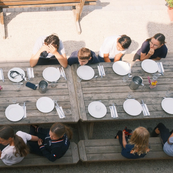 Vue de dessus d'une longue tablée dressée avec des jeunes attablés en extérieur