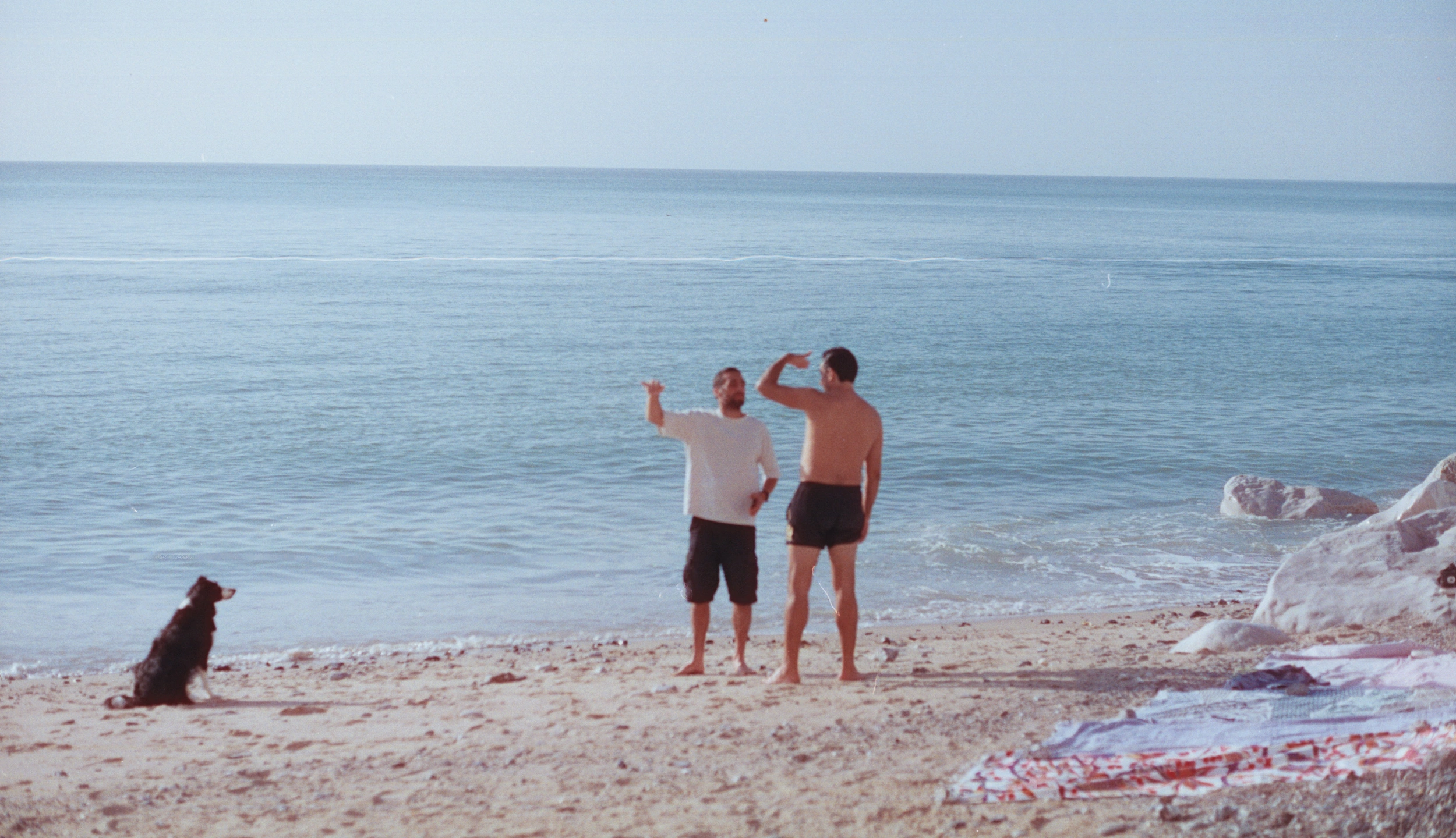 Deux hommes et un chien sur une plage face à la mer
