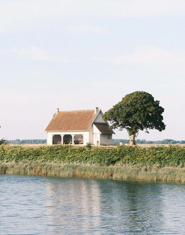Maison blanche au toit de tuiles au bord de l'eau, près d'un arbre
