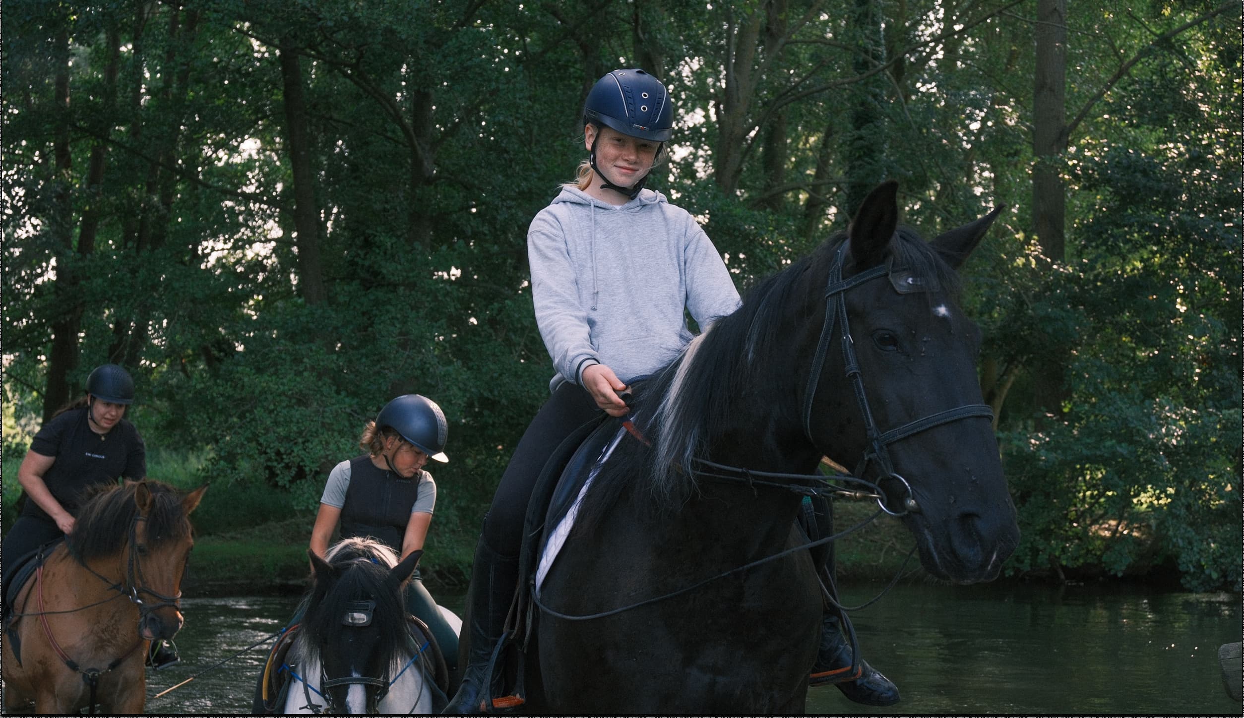 Plusieurs cavaliers traversant une rivière, une jeune fille sur un cheval noir au premier plan