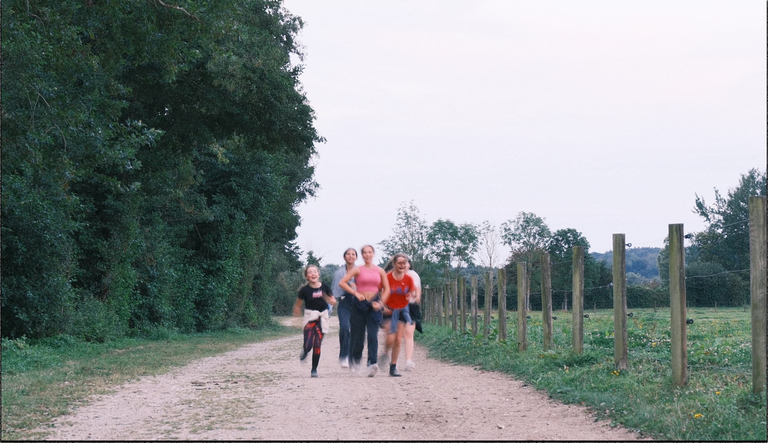 Quatre filles courant sur un chemin de terre le long d'un pré clôturé